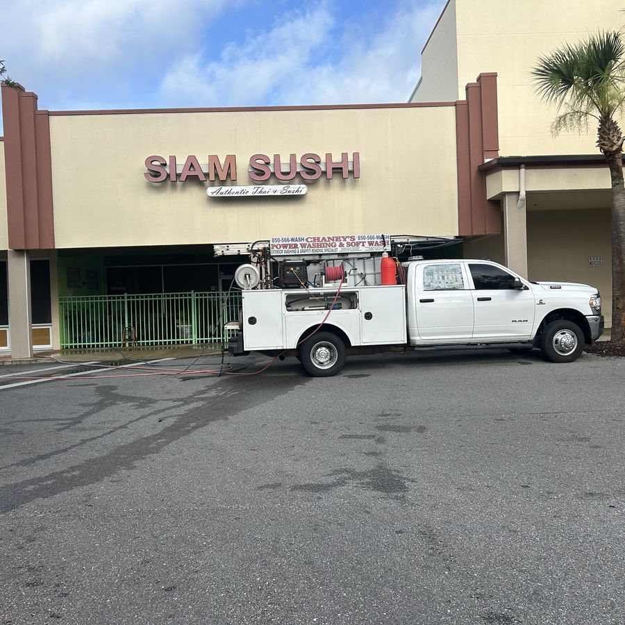 Hoses run from a Chaney's truck across freshly washed pavement in front of a shopping centre storefront.
